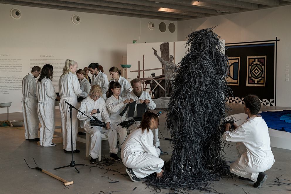 Art performance: People on white overalls are making strips of black paper and decorating a structure with the strips.