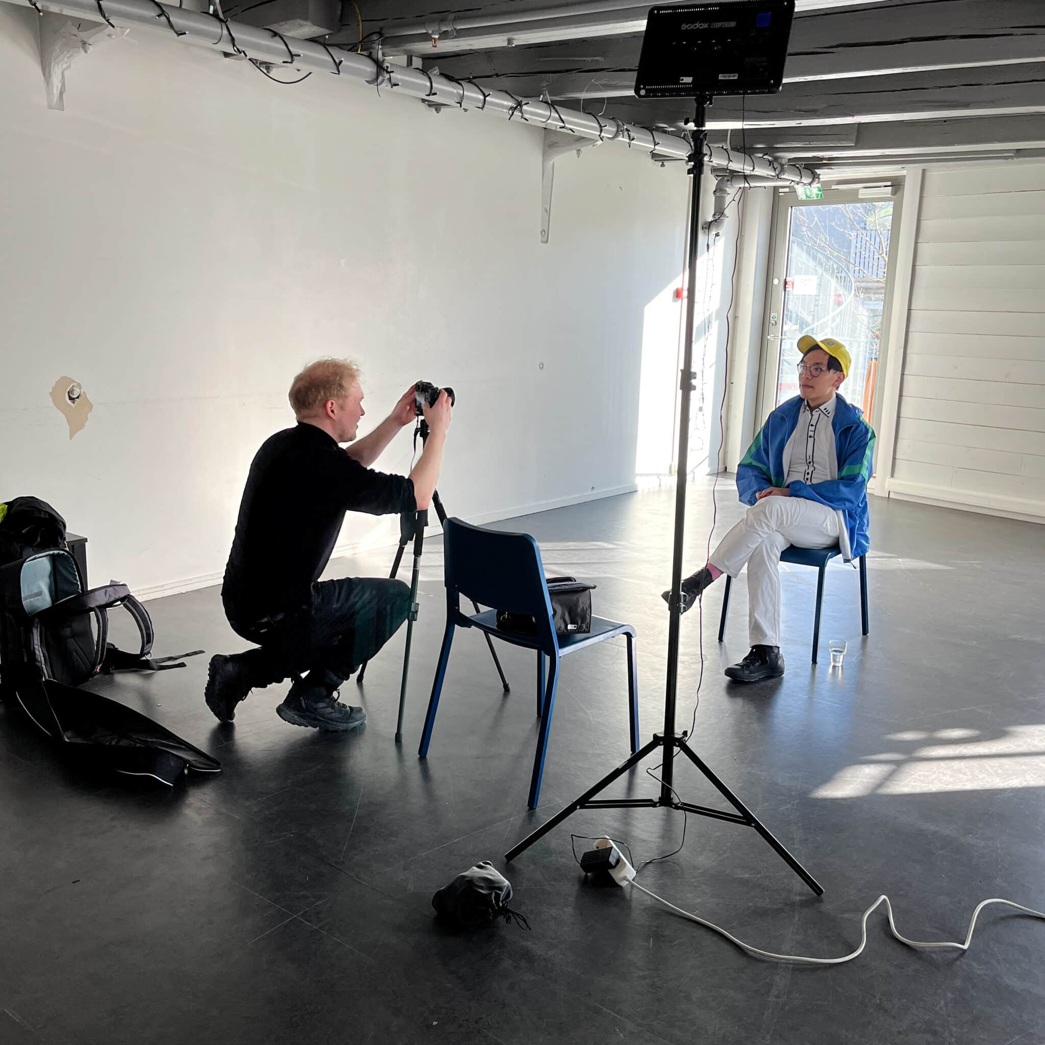 Man interviews a artist about his opera in a white room/ theatre space in Bergen, Norway.