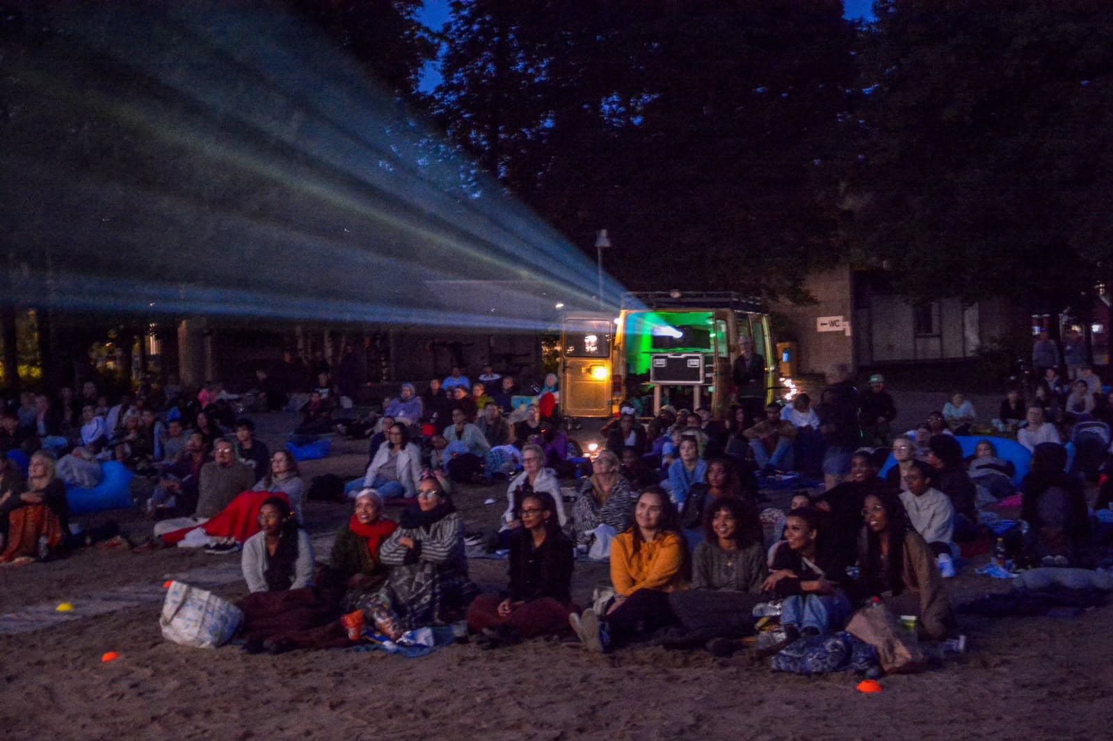 People sitting on the beach at night time with a movie projector in the background.