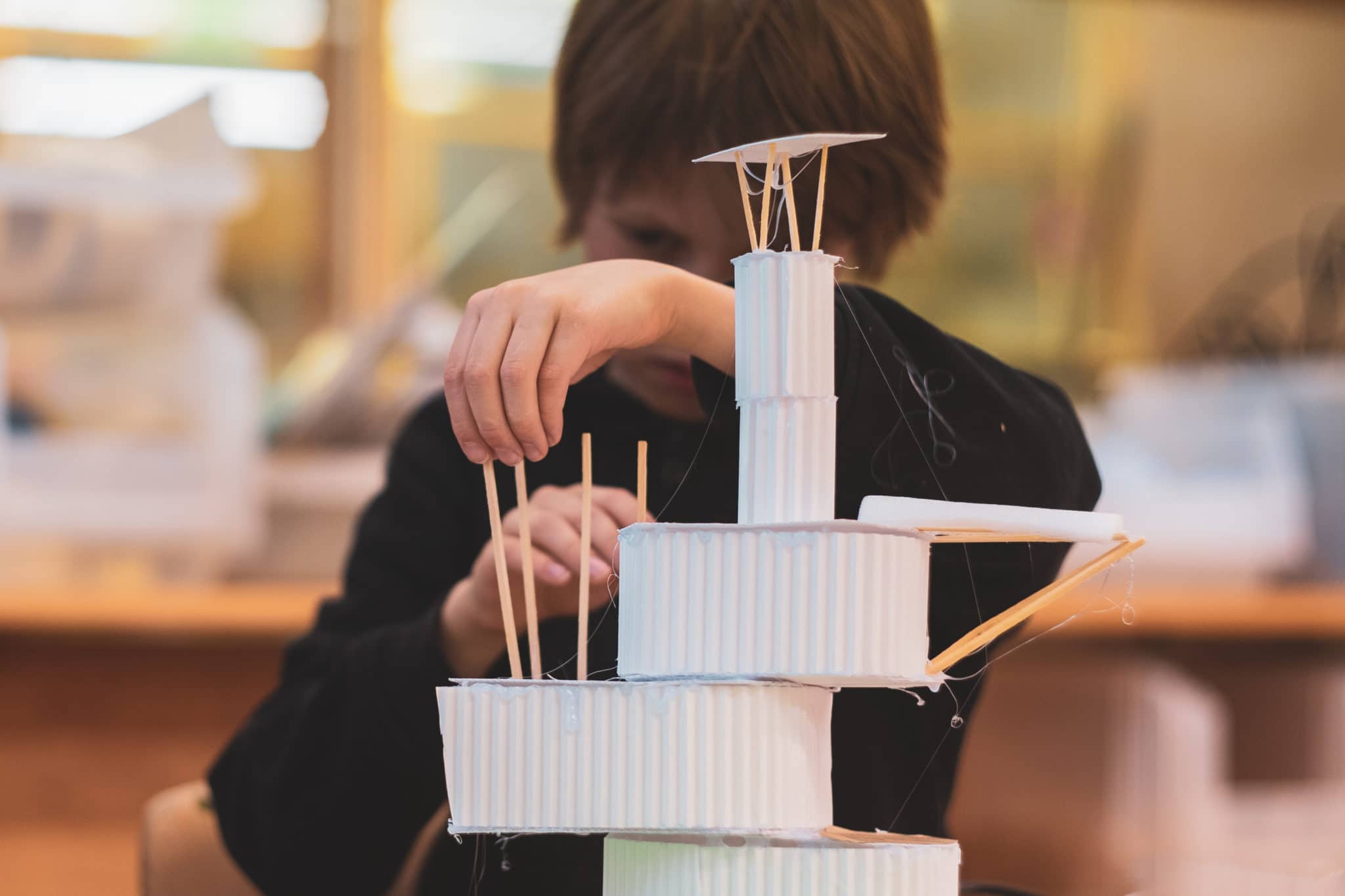 En gutt bygger hvit papirhus.