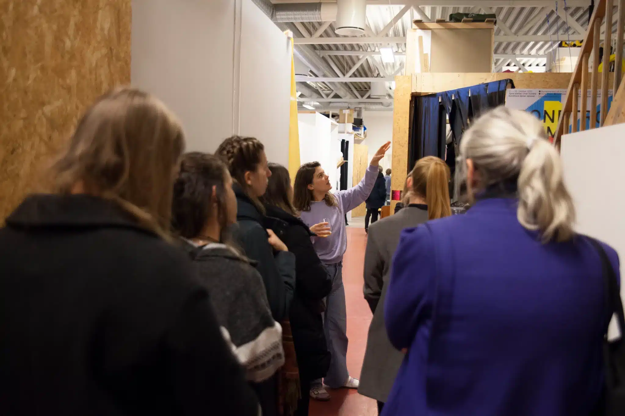 At Trondheim Open, artist Anna Liljekrantz leading a guided tour for six people in a building with a red floor and white walls as they stand attentively.