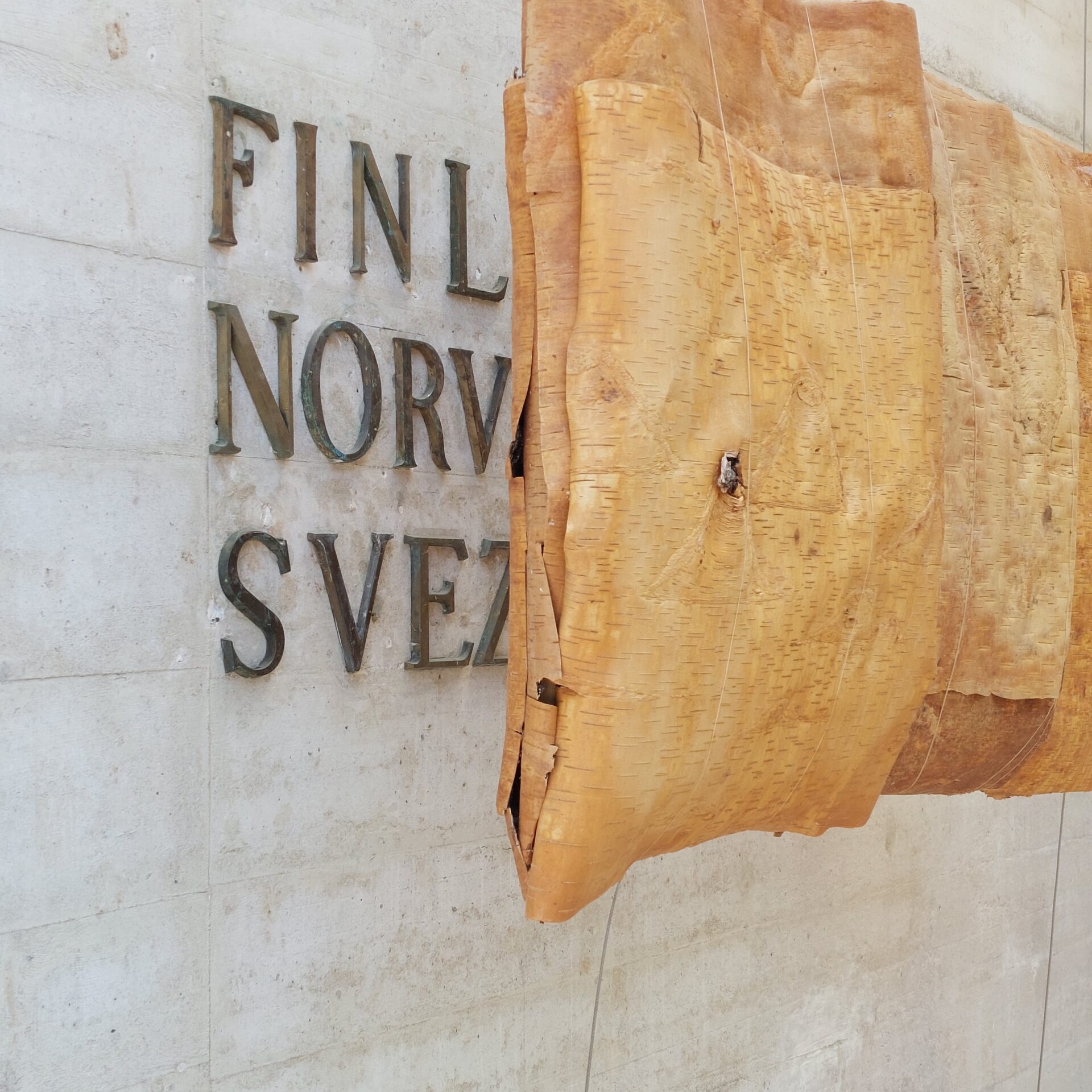 Wooden art piece covering the words Finland, Norway and Sweden, which are written with metallic letters and attached to a concrete wall.