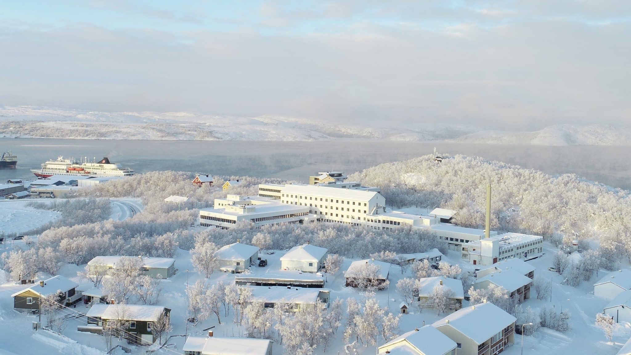 Bright winter day, aerial view of the Nothing Hill campus´ white buildings, sea and gently sloping hills in the background.