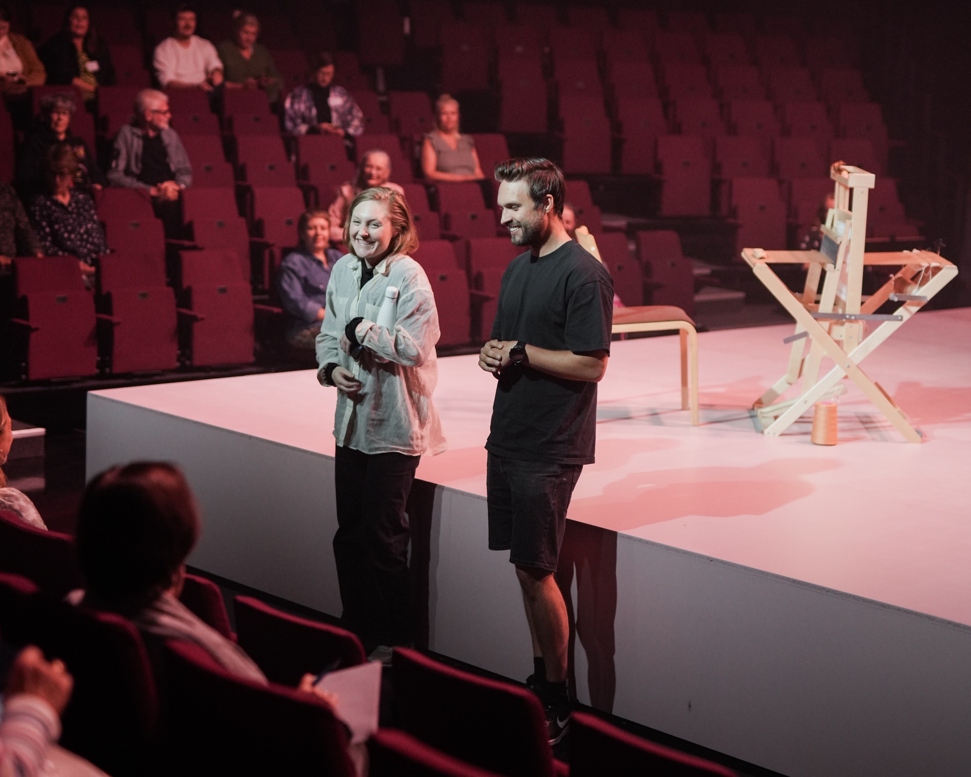 Two people standing in front of a stage, talking to audience.