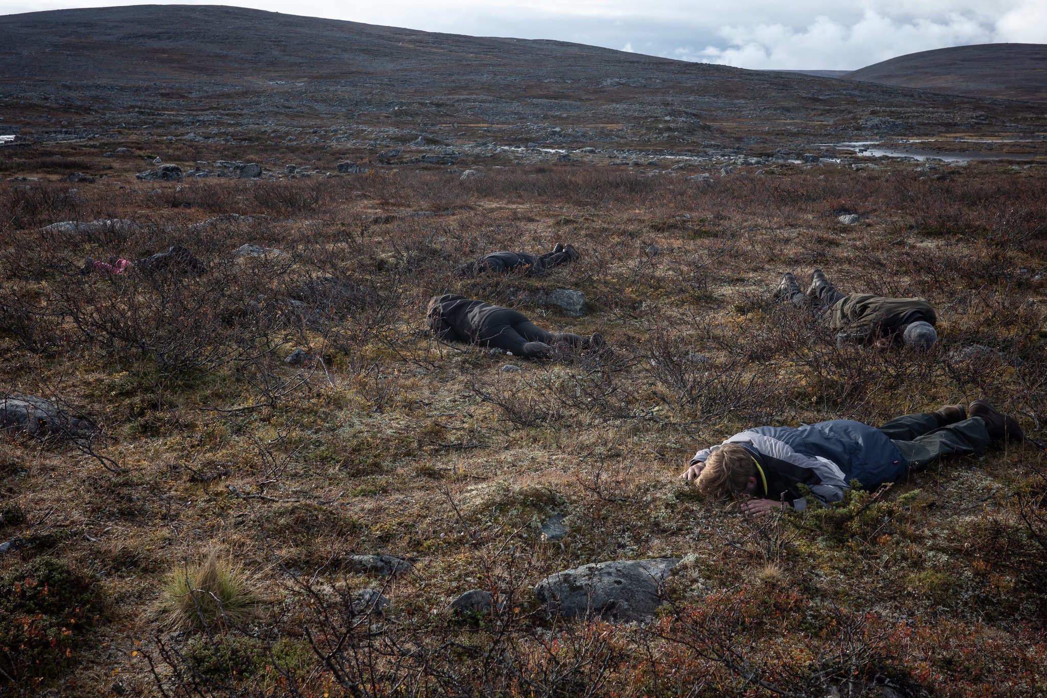 Four people lying on the ground in a mountain valley.