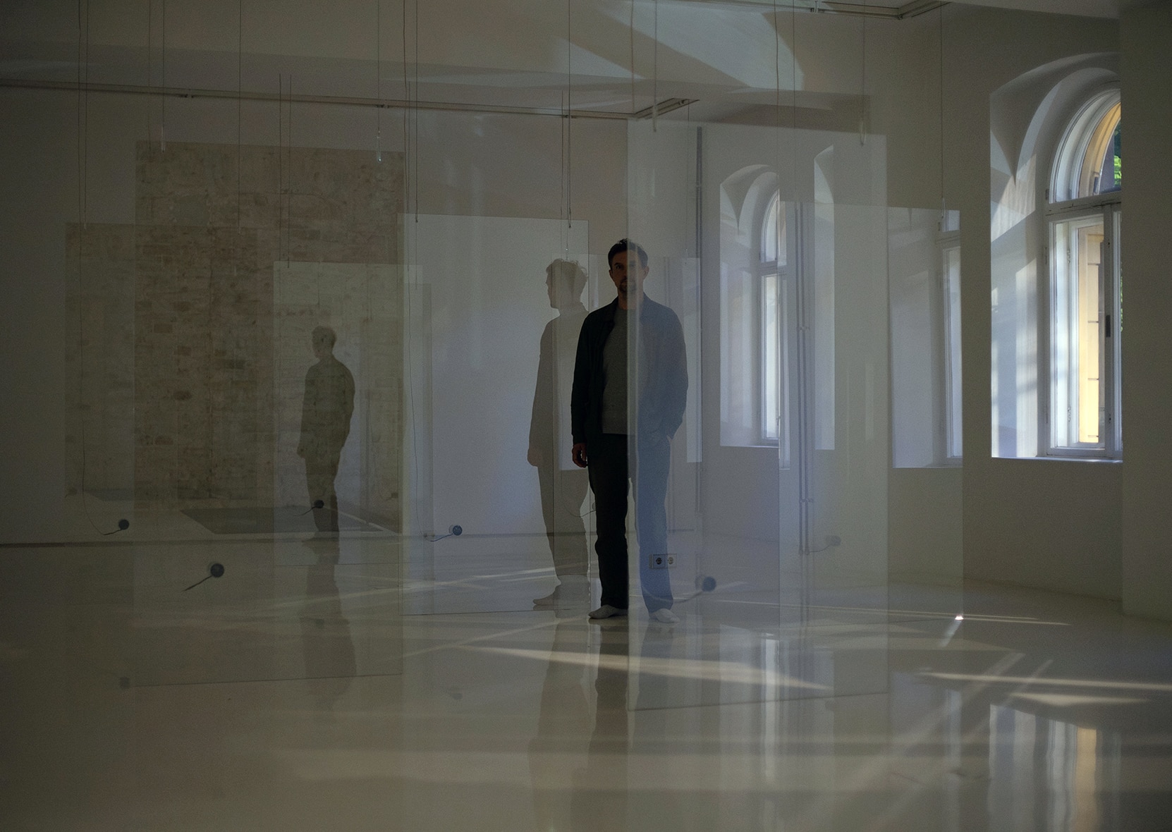 Artist Hans Rosenström is posing in a spacious white room with glass walls, filled with natural light from large windows.