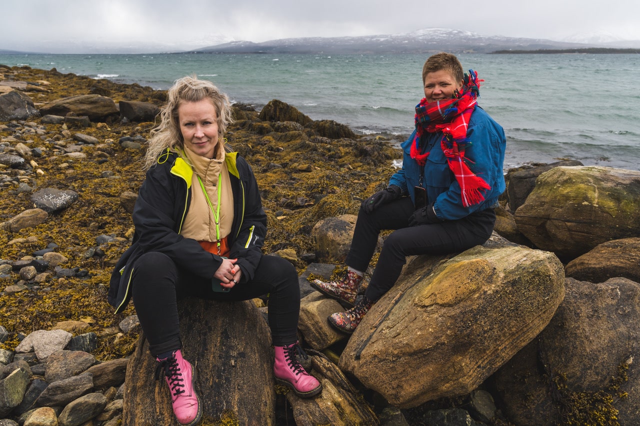 Two women sitting on big stones. The ocean is in the background.