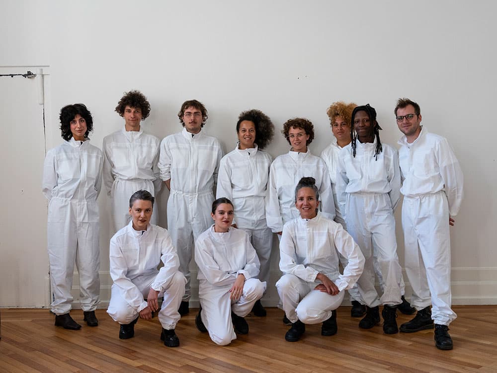 A group photo of eleven people in white overalls.