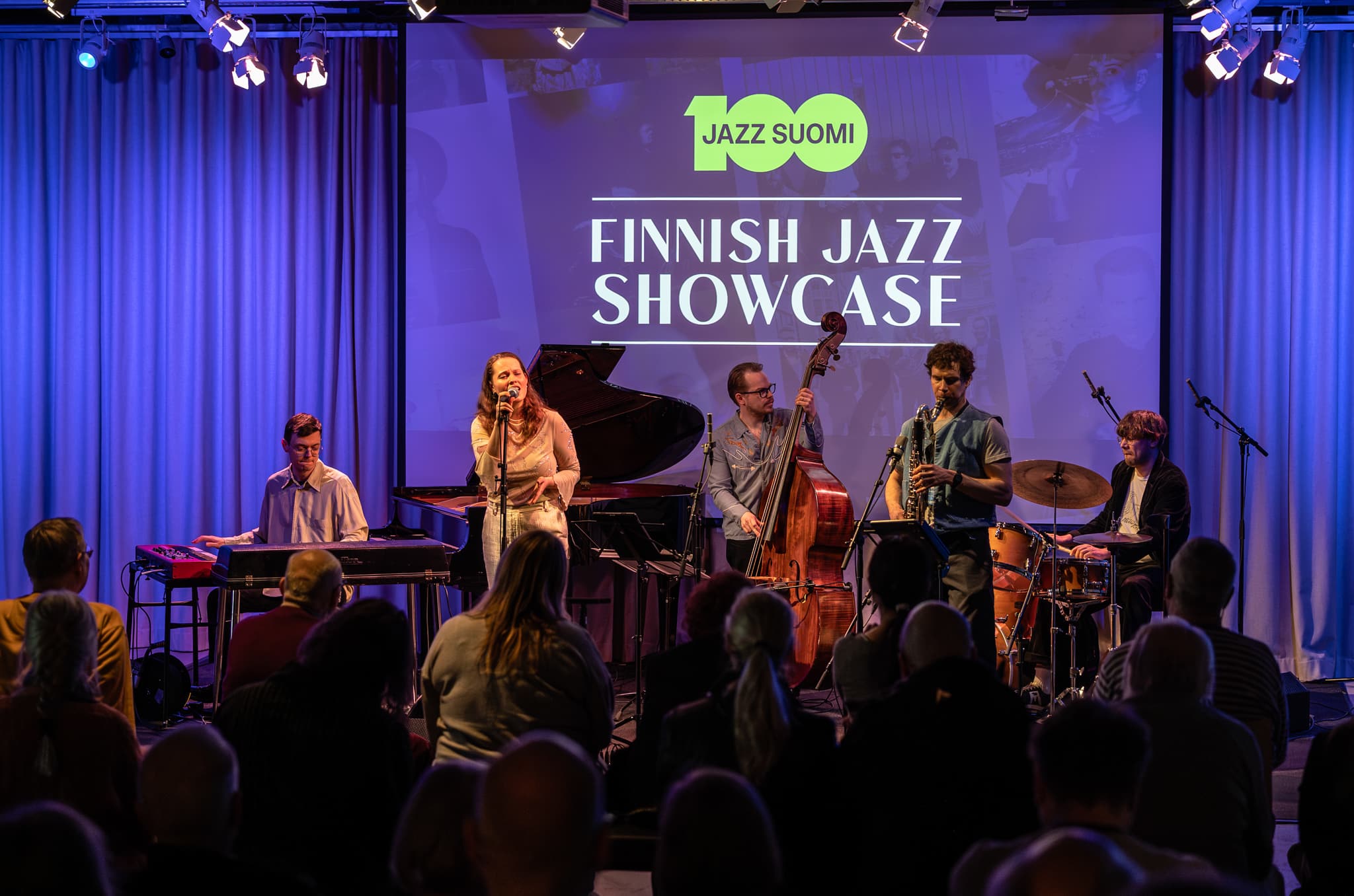 Jazz band performing on stage in front of a blue backdrop with writing "Finnish Jazz Showcase"