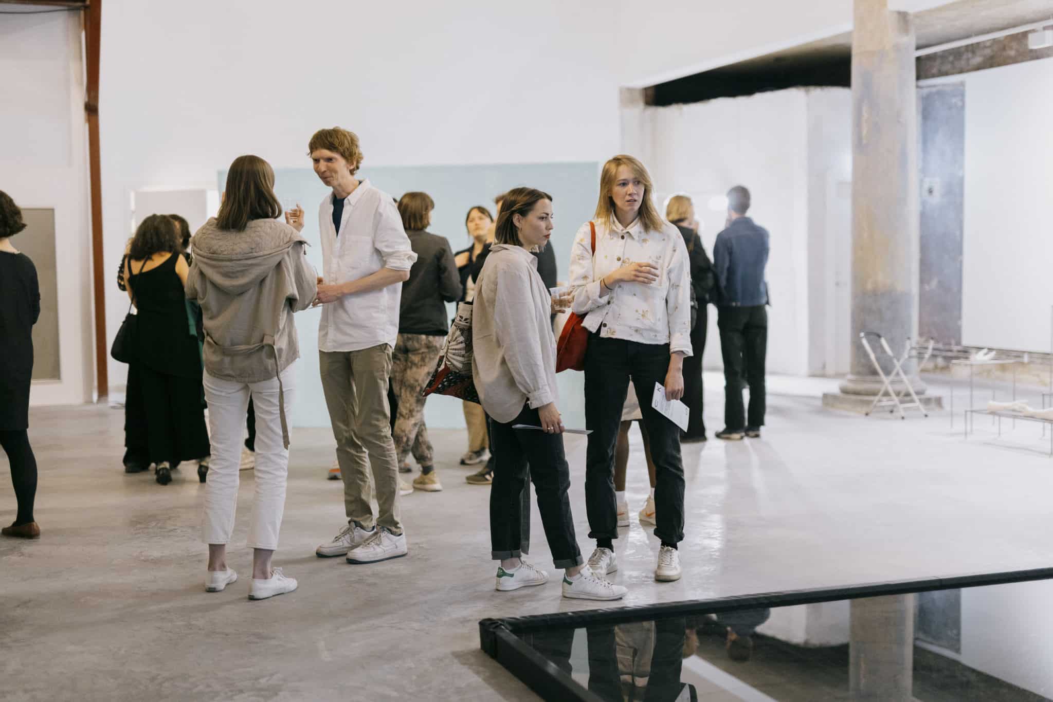 A bright art gallery space, multiple people standing and talking with eachother.
