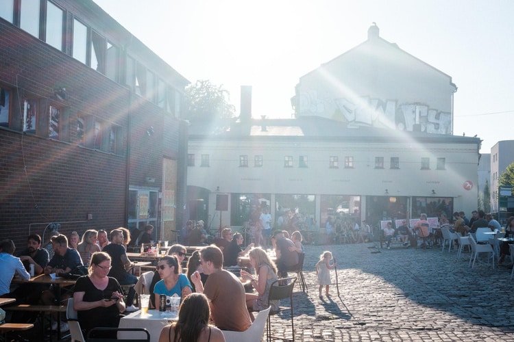 People sitting in around tables in a sunny yard.