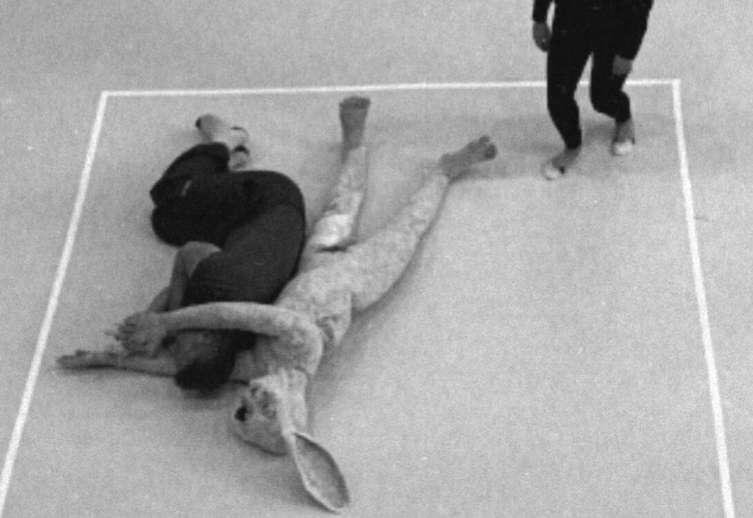 A person dressed in black and a rabbit shaped sculpture against a white floor.